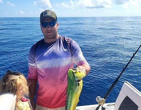 Man holding a fish on a boat with a child during a Florida Keys fishing charters trip.