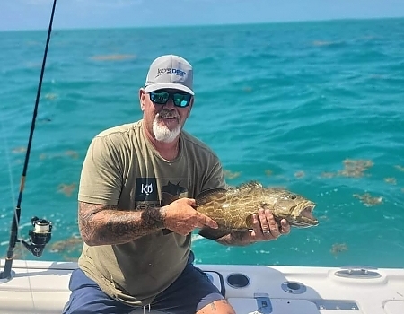 Man holding a fish on a boat in the ocean during a Key Largo fishing charters trip.