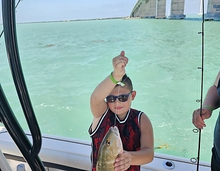 Child holding a fish on a boat with a bridge in the background in Islamorada.